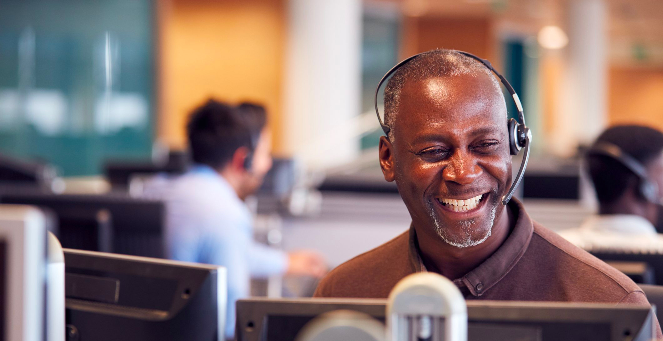 Mature Businessman Smiling Wearing Telephone Headset Talking To Caller In Customer Services Department